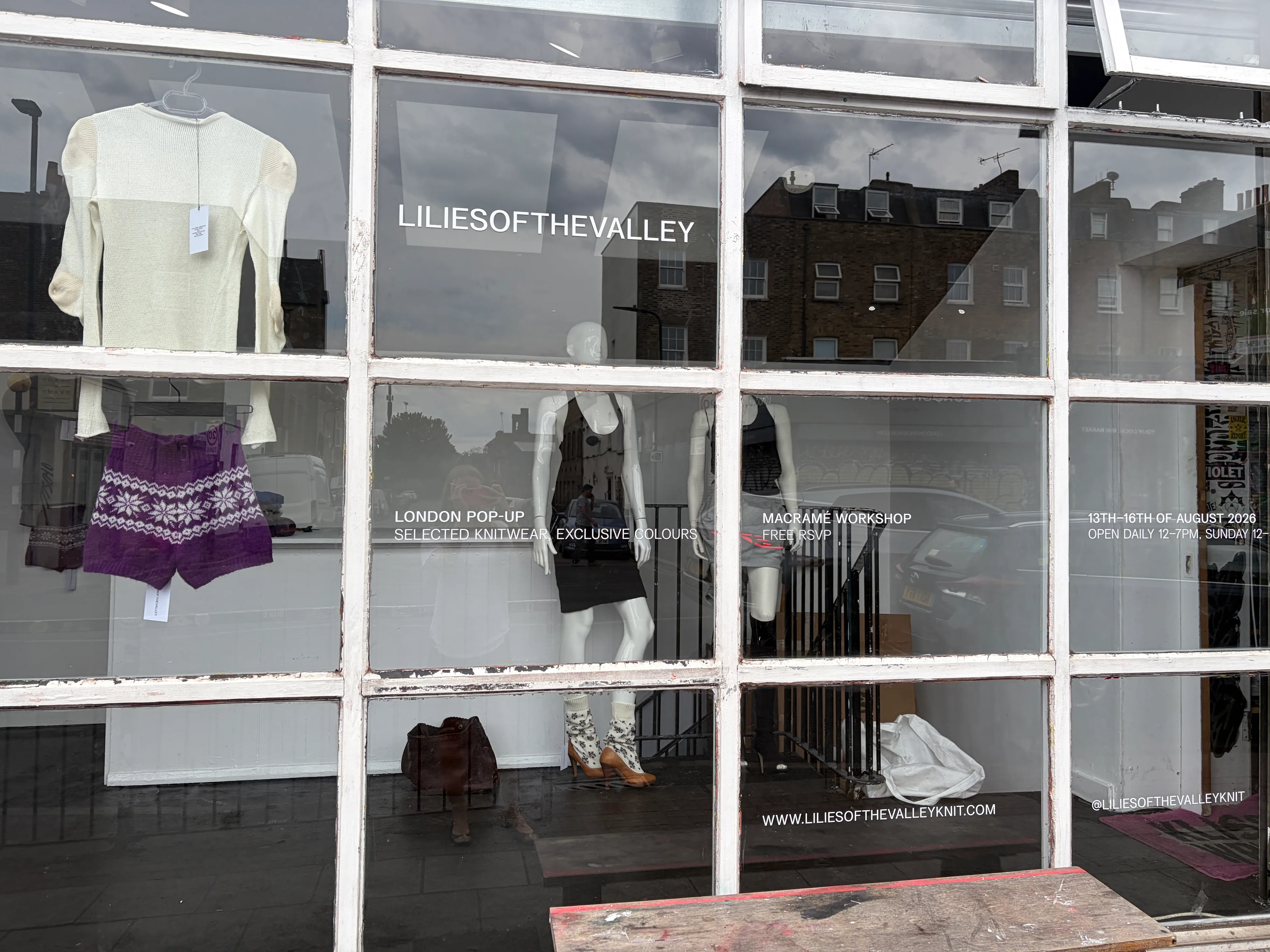 The full shopfront with knitwear hung against the glass and the dates
                    and web address set along the lower panes.