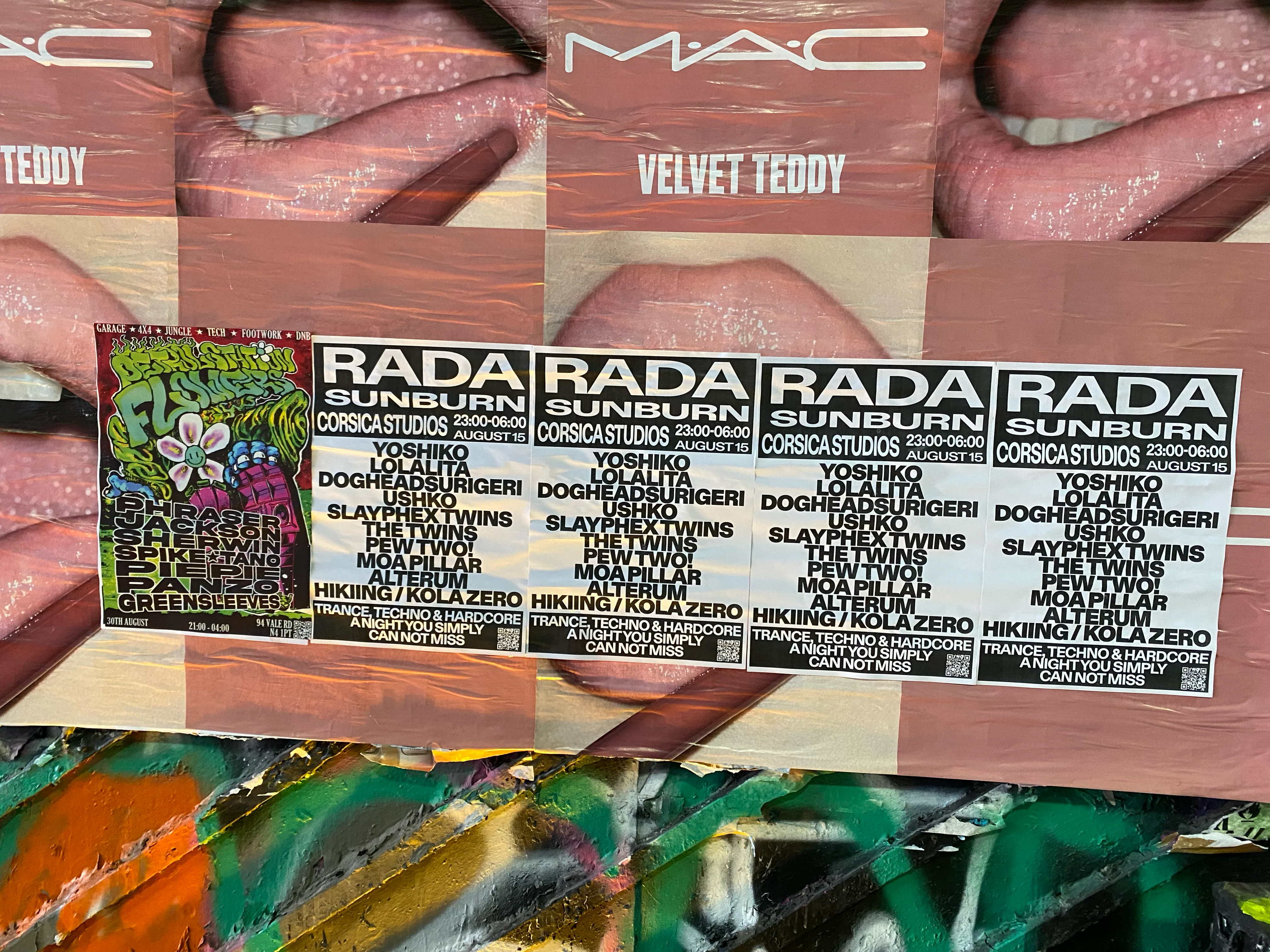 The poster flyposted in a row over a cosmetics billboard, with graffiti below.